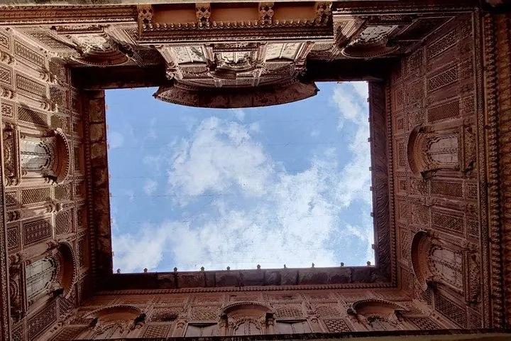 Looking straight up at a square opening of blue sky surrounded by ornate carved stone walls